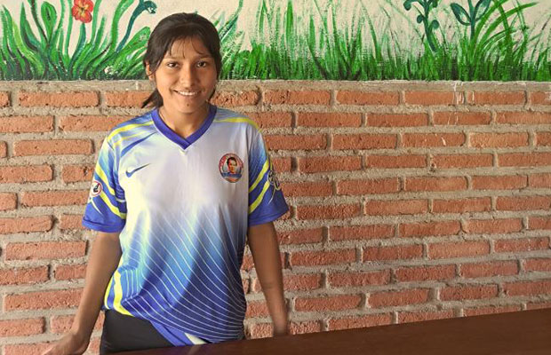 Female student standing in front of brick wall at school smiling because she is getting a new computer